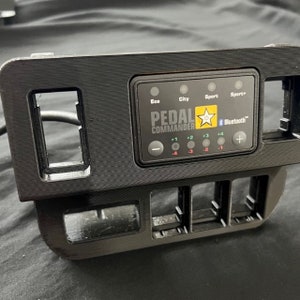 May include: Black plastic panel with a digital display labeled "Pedal Commander" with buttons for Eco, City, Sport, and Sport+ modes. The display shows Bluetooth connectivity and adjustment levels from -4 to +4.