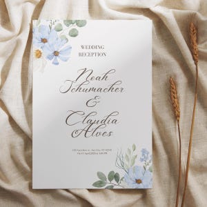 May include: A wedding reception sign with floral accents. The sign features the names "Noah Schumacher & Claudia Alves" in elegant script. The text "WEDDING RECEPTION" is at the top. The date and time are also included. The sign is decorated with blue flowers and green leaves.