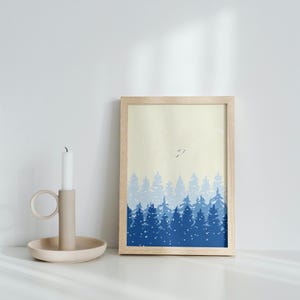 May include: A framed print of a blue and white forest scene with a light yellow background. The print features a row of trees in various shades of blue, with a few white birds flying above. The trees are silhouetted against the yellow background, creating a simple and elegant design.