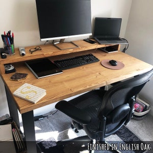 May include: A wooden desk with a black metal frame and a black office chair. The desk has a shelf for a monitor and a keyboard. The desk is finished in English Oak.