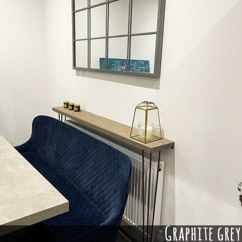 May include: A navy blue, quilted bench with a wooden shelf above a radiator. The shelf holds small jars and a gold geometric lantern with a candle. A large, dark-framed mirror hangs on the white wall above the shelf.