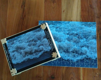 Op de afbeelding: Een handgesneden houten puzzel met 154 stukjes die een close-up van schuimend water tonen. De puzzel is getiteld "Frothing Water" door Kevin Quillen.
