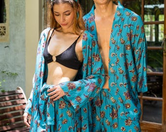 Puede incluir: Una pareja vistiendo pijamas a juego de estampado floral azul y dorado. La mujer lleva un sujetador negro debajo de su top. El hombre lleva una bata con estampado floral.