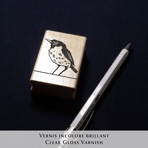 A rubber stamp with an illustration of a bird and the text EX LIBRIS CLEMENT SCARPI rests beside its stamped impression on a book page, making a parfait cadeau fait main for collectors of bijoux uniques or vintage treasures.