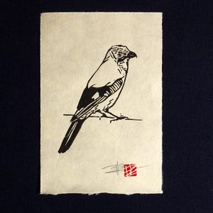 May include: A monochrome linocut print featuring a bird perched on a thin branch. The bird is rendered in black ink with detailed linework. A small red square and signature are in the lower right corner of the print.