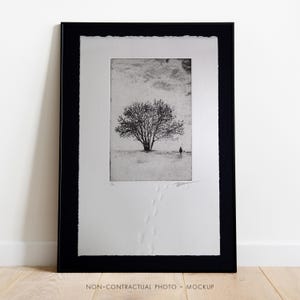 Puede incluir: Impresión enmarcada en blanco y negro de un árbol con una sola figura que se aleja en la distancia. Las huellas conducen desde el árbol hacia la nieve.
