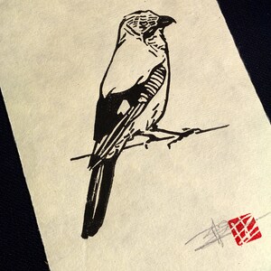 May include: A monochrome linocut print featuring a bird perched on a branch. The bird is rendered in a minimalist style with strong lines and a textured effect. A red square stamp is in the lower right corner. The print is on cream-coloured paper.