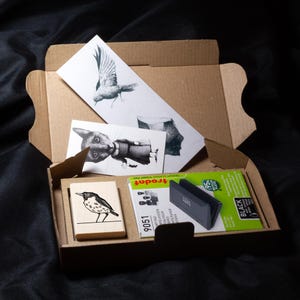 A rubber stamp with an illustration of a bird and the text EX LIBRIS CLEMENT SCARPI rests beside its stamped impression on a book page, making a parfait cadeau fait main for collectors of bijoux uniques or vintage treasures.