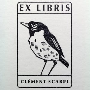 A rubber stamp with an illustration of a bird and the text EX LIBRIS CLEMENT SCARPI rests beside its stamped impression on a book page, making a parfait cadeau fait main for collectors of bijoux uniques or vintage treasures.
