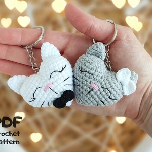 May include: Two crocheted cat keyrings in the shape of hearts. One is white with a black bow tie and the other is grey.  PDF crochet pattern.