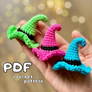 Puede incluir: Tres sombreros de bruja de ganchillo en diferentes colores: verde, rosa y azul. Los sombreros tienen un ribete negro y se sostienen en una mano. La imagen incluye el texto "PDF crochet pattern".