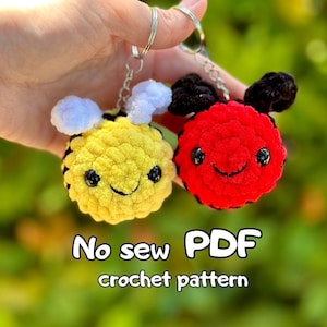 May include: Crochet pattern PDF for a bee and ladybug keychain. The bee is yellow with black stripes and white wings. The ladybug is red with black spots and black antennae. No sew pattern.
