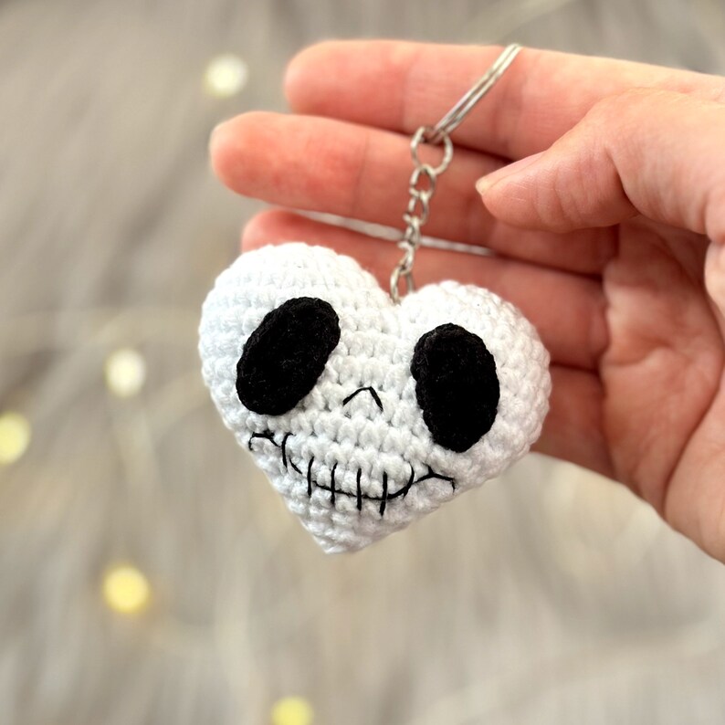May include: White crocheted heart-shaped keychain with a black skull face and a silver chain.