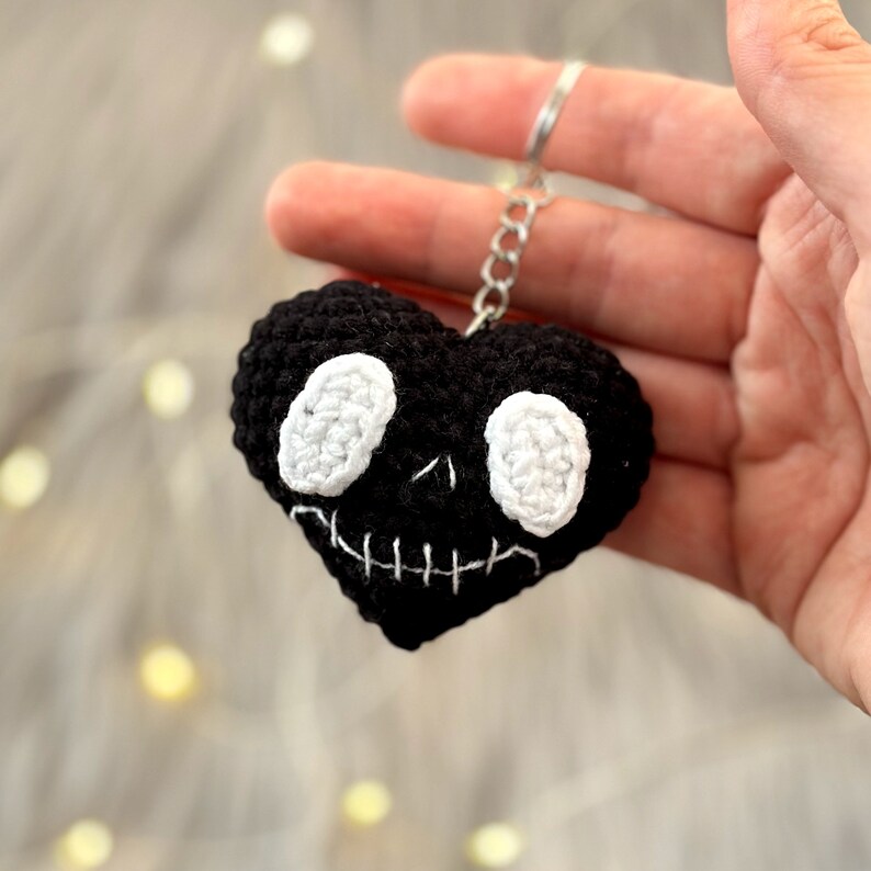 May include: Black crocheted heart-shaped keychain with a white skull face and stitched mouth.