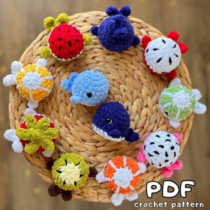 May include: A collection of colorful, crocheted sea creatures, including turtles and whales, arranged on a woven mat. The creatures are in various colors such as blue, red, white, green, and orange. The image includes the text "PDF crochet pattern".