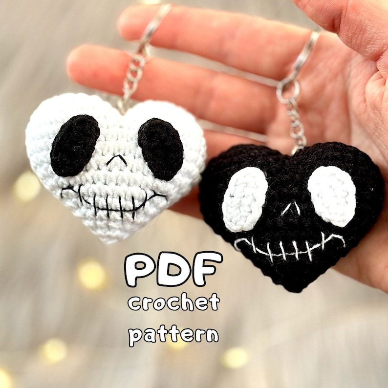 May include: Two crocheted heart-shaped keychains with a skull design. One keychain is white with black details, and the other is black with white details. The text "PDF crochet pattern" is below the keychains.