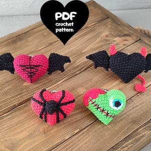 May include: Four crocheted heart-shaped ornaments with different Halloween themes. The ornaments are red, black, green, and red with black accents. The ornaments are on a wooden surface. The text "PDF crochet pattern" is on a black heart-shaped background.