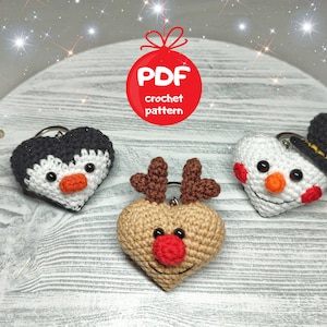 May include: Three crocheted heart-shaped ornaments: a penguin, a snowman wearing a black top hat, and a reindeer. The ornaments are on a wooden surface. PDF crochet pattern.