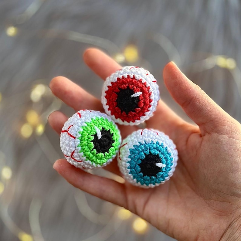 May include: Three crocheted eyeballs with different colored irises: red, green, and blue. The eyeballs are white with red veins and black pupils.