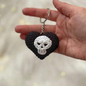 Puede incluir: Un llavero en forma de coraz&oacute;n negro tejido a ganchillo con un dise&ntilde;o de calavera blanca. El llavero est&aacute; hecho de hilo y tiene un anillo de metal plateado. La calavera est&aacute; centrada en el coraz&oacute;n.