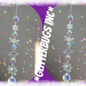 May include: A celestial-themed suncatcher with a chain, featuring a star, moons, planets, and a sun pendant. The suncatcher has iridescent crystal spheres and a large crystal at the bottom. The text "*GLITTERBUGS INC*" is visible.