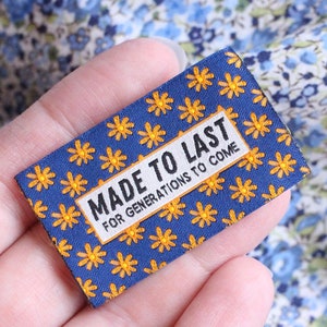May include: A blue fabric label with a yellow daisy pattern and the text "MADE TO LAST FOR GENERATIONS TO COME".