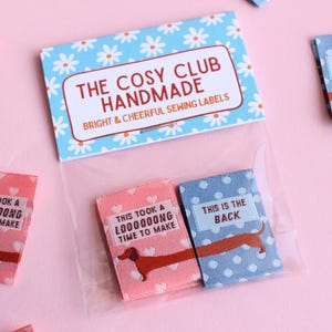 May include: A package of handmade sewing labels with a dachshund illustration. The labels are pink and blue with white polka dots and hearts. The text on the labels reads "THIS IS THE BACK" and "THIS TOOK A LOOOOOONG TIME TO MAKE".