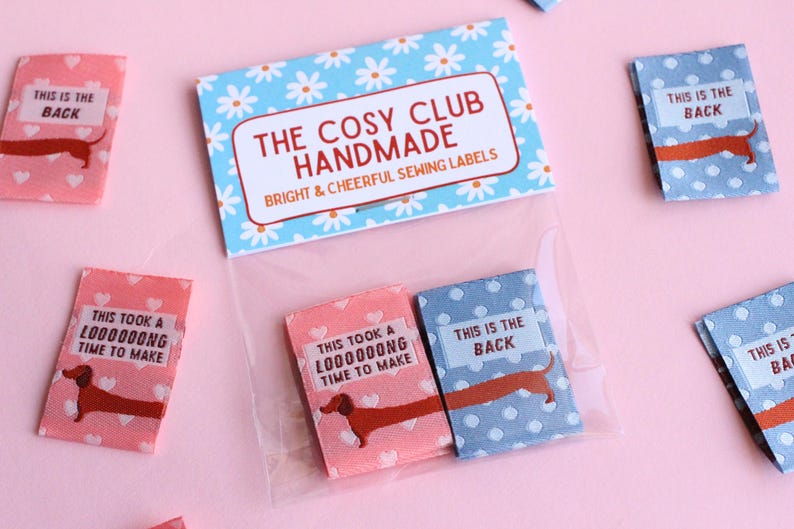 May include: A package of handmade sewing labels with a dachshund illustration. The labels are pink and blue with white polka dots and hearts. The text on the labels reads "THIS IS THE BACK" and "THIS TOOK A LOOOOOONG TIME TO MAKE".
