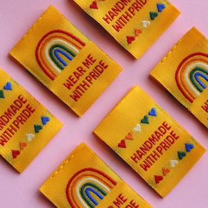 May include: Six yellow fabric labels with rainbow and heart designs. The labels have the text "Handmade with Pride" and "Wear Me With Pride" on them.