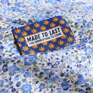 May include: A blue fabric with a white floral pattern. A blue and yellow label with the text "Made to Last for Generations to Come" is attached to the fabric.