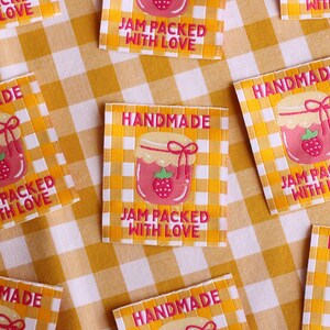 May include: Square labels with a yellow and white checkered background. Each label features a pink jar of jam with a strawberry and the words "HANDMADE" and "JAM PACKED WITH LOVE" in a pink font.