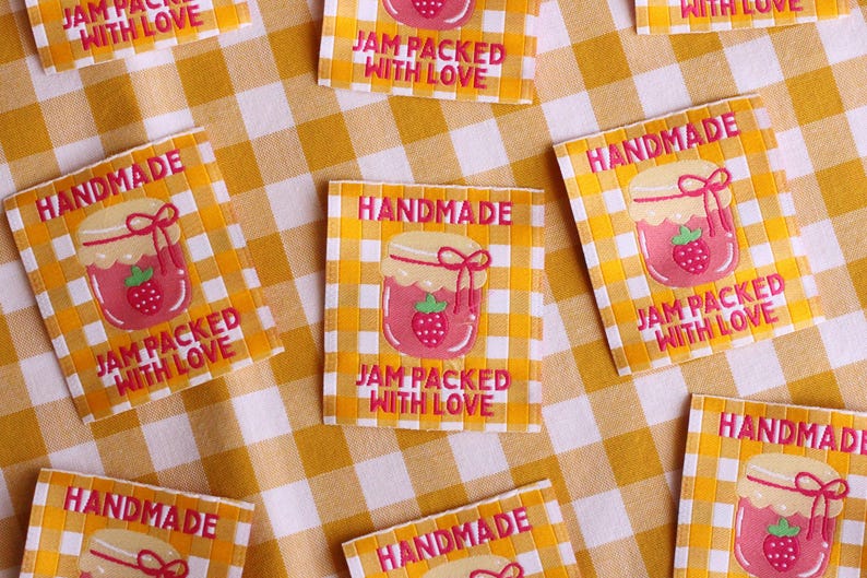 May include: Square labels with a yellow and white checkered background. Each label features a pink jar of jam with a strawberry and the words "HANDMADE" and "JAM PACKED WITH LOVE" in a pink font.
