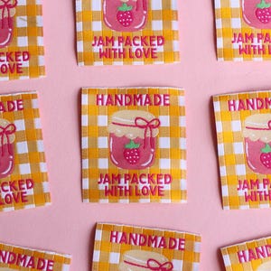 May include: Square fabric labels with a yellow and white checkered pattern. Each label features a pink jar of jam with a strawberry and the text "JAM PACKED WITH LOVE" and "HANDMADE" in pink.