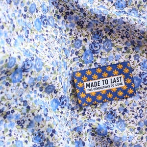 May include: A blue and yellow fabric label with white text that reads "Made to Last for Generations to Come". The label is on a white fabric with a blue floral pattern.