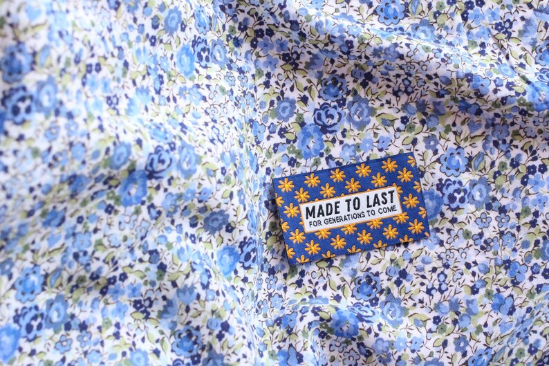 May include: A blue and yellow fabric label with white text that reads "Made to Last for Generations to Come". The label is on a white fabric with a blue floral pattern.