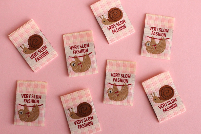 Peut inclure: Huit &eacute;tiquettes en tissu vichy rose et blanc avec des paresseux et des escargots brod&eacute;s. Les &eacute;tiquettes indiquent "Very Slow Fashion".