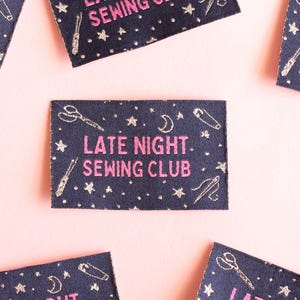 May include: Navy blue fabric patches with the text "LATE NIGHT. SEWING CLUB" in pink. The patches are decorated with embroidered scissors, needles, and stars. The background is a pale pink.