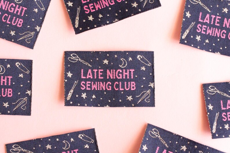 May include: Navy blue fabric patches with the text "LATE NIGHT. SEWING CLUB" in pink. The patches are decorated with embroidered scissors, needles, and stars. The background is a pale pink.