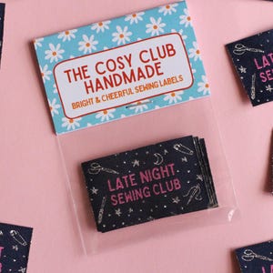 May include: Sewing labels with the text "LATE NIGHT SEWING CLUB" in pink on a dark blue background. The labels feature illustrations of scissors, needles, and moons. The packaging reads "THE COSY CLUB HANDMADE" with a floral design.