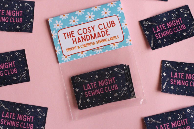 May include: Sewing labels with the text "LATE NIGHT SEWING CLUB" in pink on a dark blue background. The labels feature illustrations of scissors, needles, and moons. The packaging reads "THE COSY CLUB HANDMADE" with a floral design.