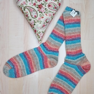 May include: A pair of striped socks in shades of blue, red, and grey. A heart-shaped cushion with a floral paisley pattern is also in the image. The socks are on a light wood surface.