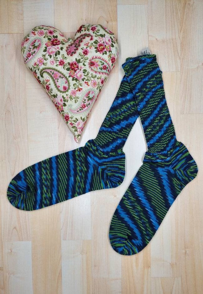 Puede incluir: Un par de calcetines a rayas azules y verdes con una almohada floral en forma de coraz&oacute;n sobre una superficie de madera.