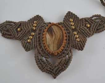 May include: A brown macrame necklace with a large oval-shaped stone pendant. The stone is brown and white with a marbled pattern. The necklace is decorated with small gold beads.