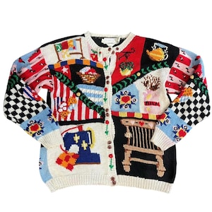 Könnte beinhalten: Eine mehrfarbige Strickjacke mit Knöpfen und verschiedenen gestickten Aufnähern. Die Aufnäher zeigen eine Nähmaschine, einen Stuhl und andere dekorative Elemente. Die Ärmel haben ein schwarz-weißes Schachbrettmuster und florale Designs.