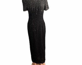 May include: A black, floor-length evening gown with short sleeves. The dress is covered in sequins that fade from silver at the shoulders to black. The dress has a round neckline and a fitted silhouette.