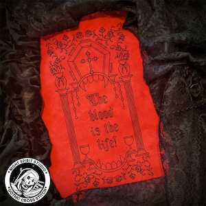 May include: A red cross stitch pattern with a gothic design featuring a coffin, roses, and the text "The blood is the life!"