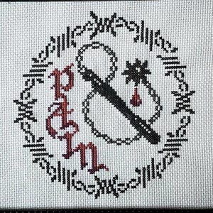 Könnte beinhalten: Schwarz gerahmte Kreuzstichkunst mit dem Wort „Pain“ in roter gotischer Schrift und einem schwarz-weißen Design aus Peitsche, Stern und Blutstropfen. Die Kunst ist von einem schwarz-weißen floralen Design umgeben.