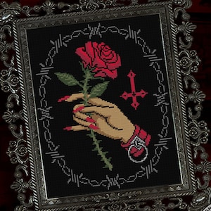 Könnte beinhalten: Kreuzstich-Muster mit einer Hand, die eine rote Rose mit Dornen, ein Kreuz und Stacheldraht hält. Das Muster ist in einem silbernen Rahmen gerahmt.
