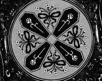 May include: Black and white cross stitch pattern of four coffins in a circular design, framed in a black ornate frame.
