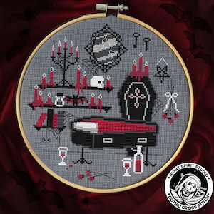 May include: A cross stitch pattern featuring a gothic-themed scene with a coffin, candles, and a skull. The pattern is framed in a wooden hoop and includes the text "Night Spirit Studio Gothic Cross Stitch".